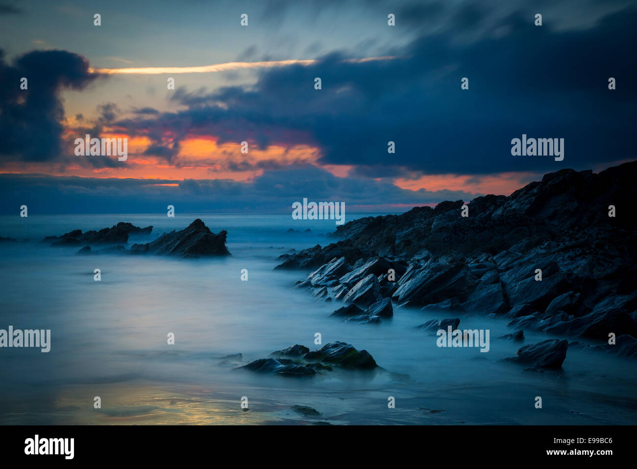 Nuvoloso Tramonto su scogli lungo la costa della Cornovaglia vicino a Newquay, Cornwall, Inghilterra Foto Stock