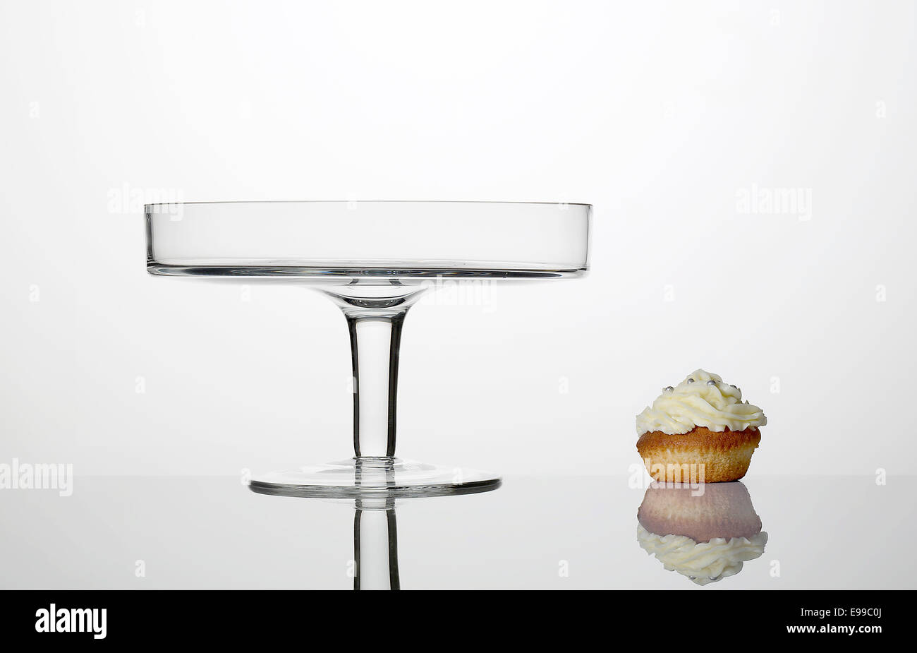 Elevato La chiave fotografia di una torta di vetro dotato di supporto con una tortina e le loro riflessioni al di sotto di esse. Foto Stock