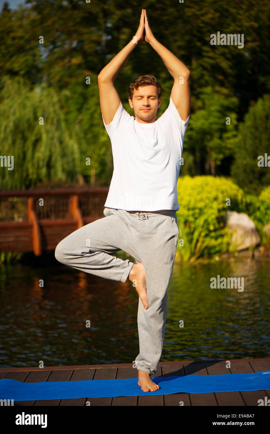 Giovane uomo la pratica dello yoga, facendo la posizione dell'albero Foto Stock