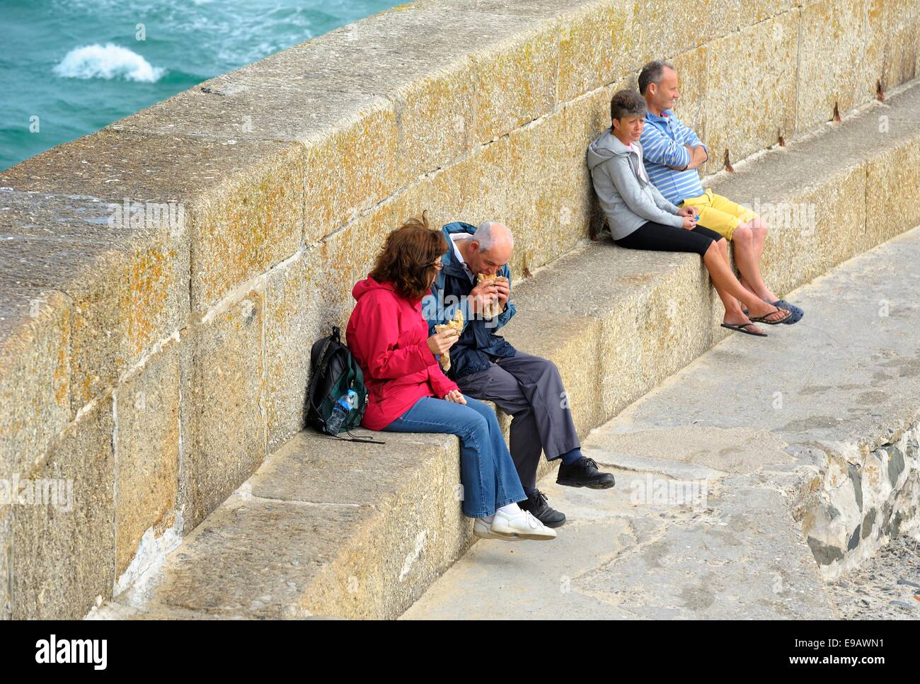 Persone mangiare e seduti sulle mura sul mare in St ives Cornwall Inghilterra Regno Unito Foto Stock