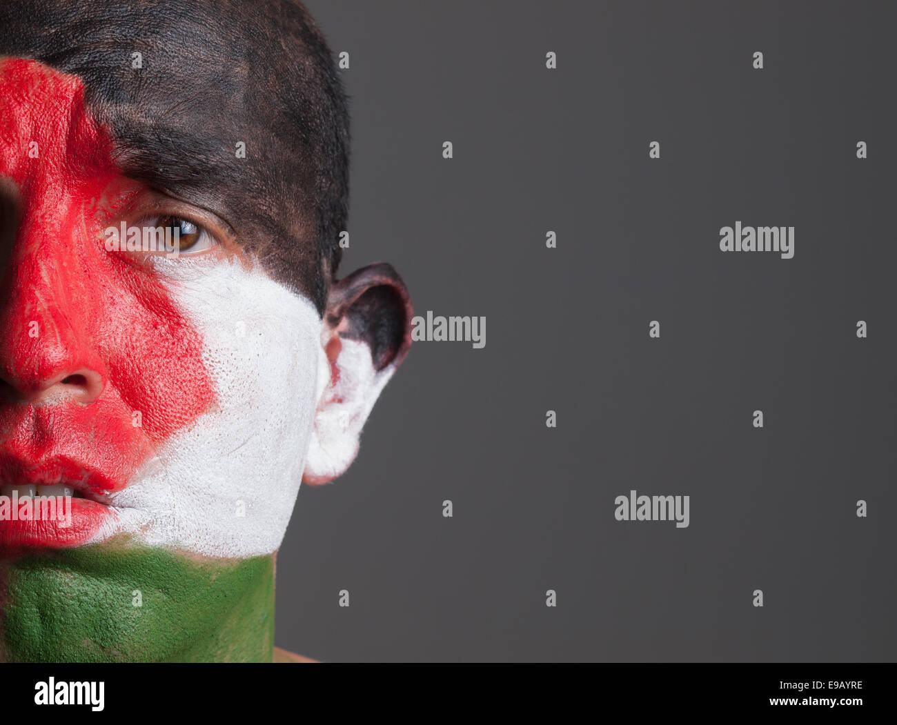 Triste l uomo e il suo volto dipinto con la Palestina bandiera. L'uomo è isolato su sfondo scuro. Foto Stock