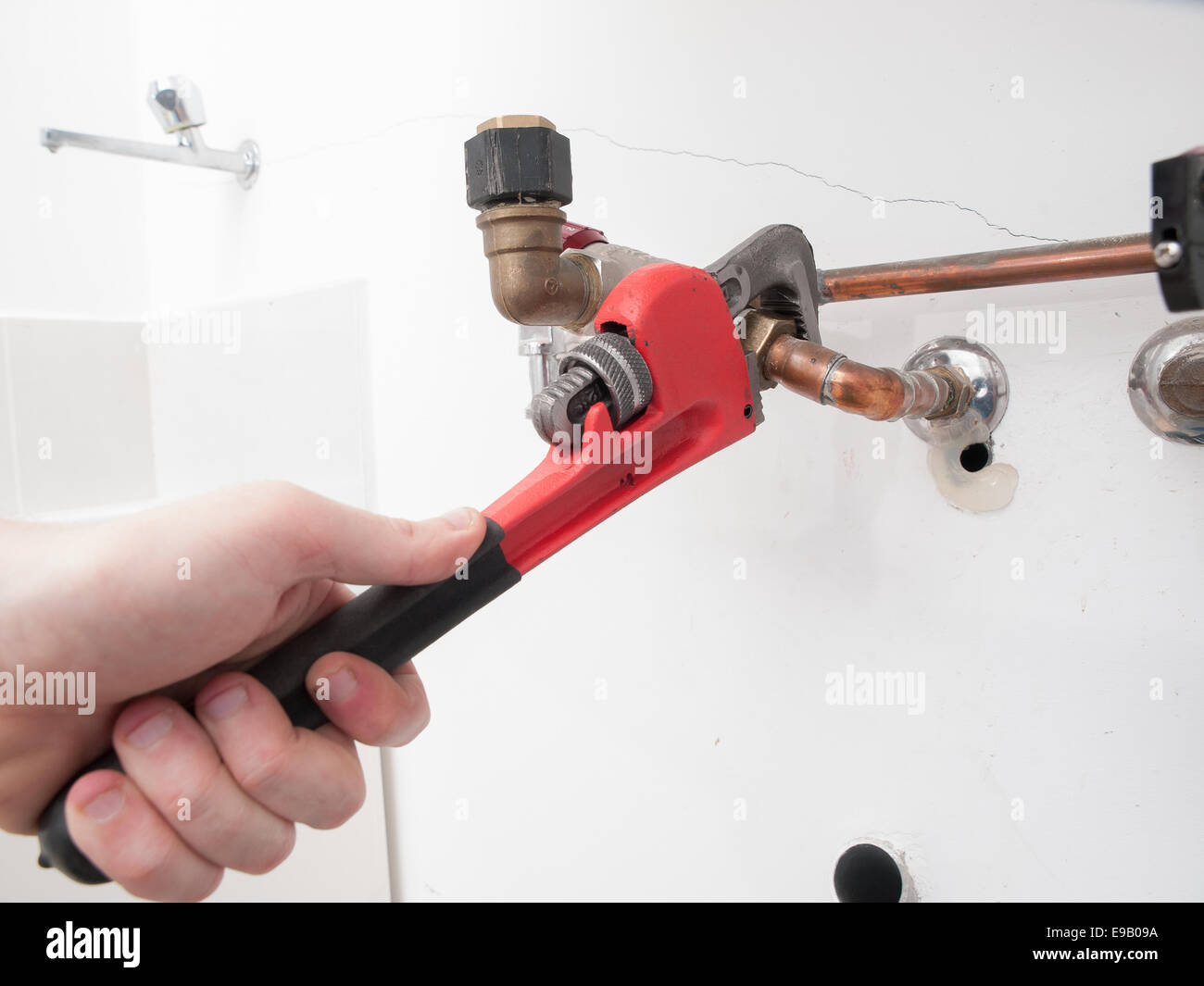 Le mani la riparazione dei tubi idraulici di un boiler elettrico con una chiave stilson Foto Stock