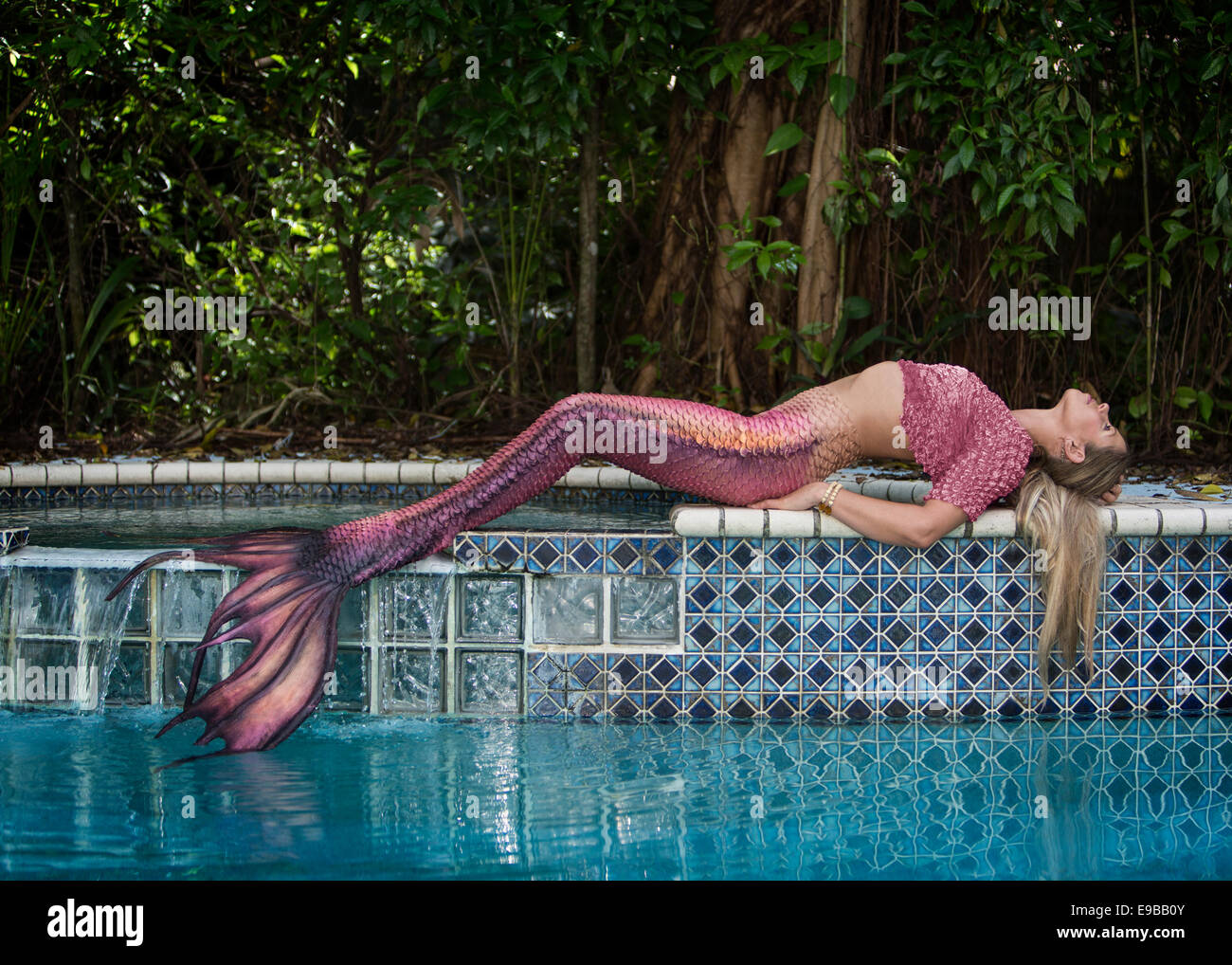 Blonde mermaid posa in opera sulla parete off una giungla piscina. Foto Stock
