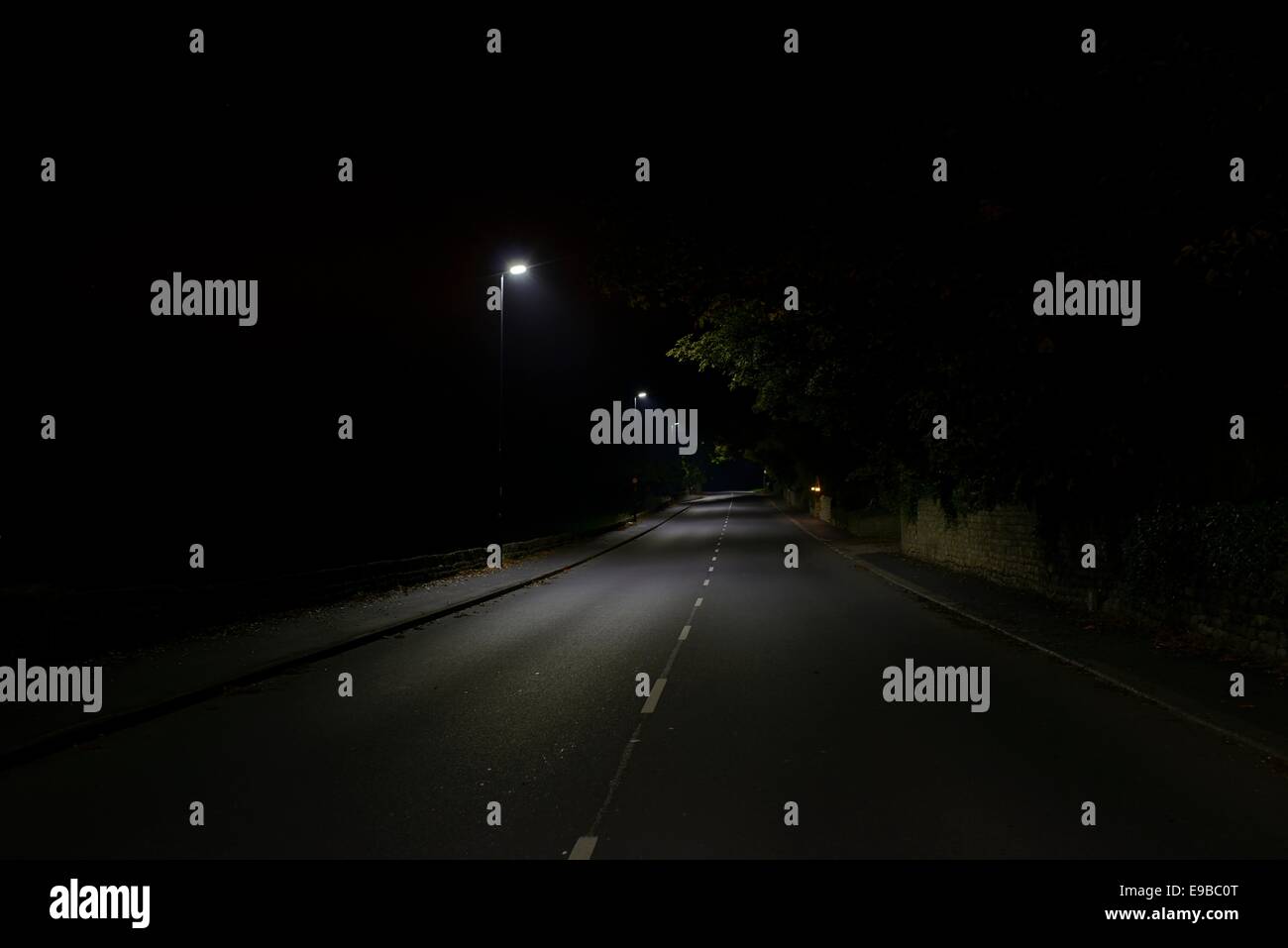 Una strada suburbana di notte, illuminato da luci a LED, con campi nelle tenebre dietro Foto Stock