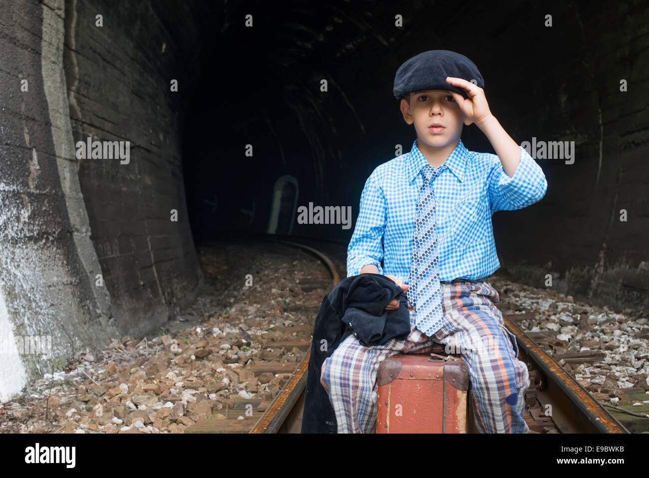 Bambino in abiti vintage siede su strada ferrata nella parte anteriore di un tunnel. Foto Stock