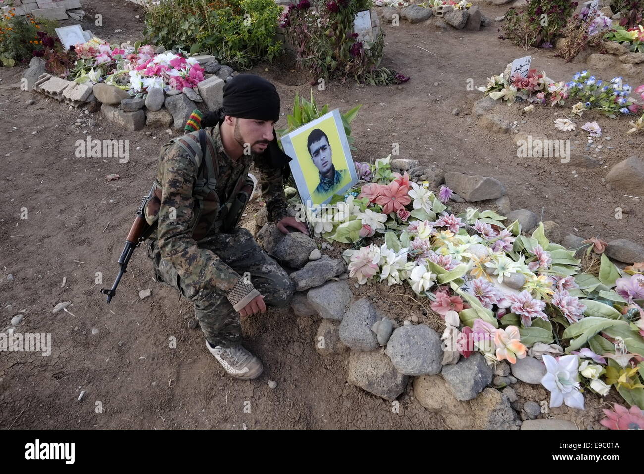 Un combattente curdo del popolo della unità di protezione YPG siede accanto a una tomba di un combattente di curdi uccisi da uno Stato islamico ISIS o ISIL militanti in un cimitero vicino la città di Al-Malikiyah anche chiamato Derek ( ) curda in Al Hasakah o distretto Hassakeh nella Siria settentrionale Foto Stock