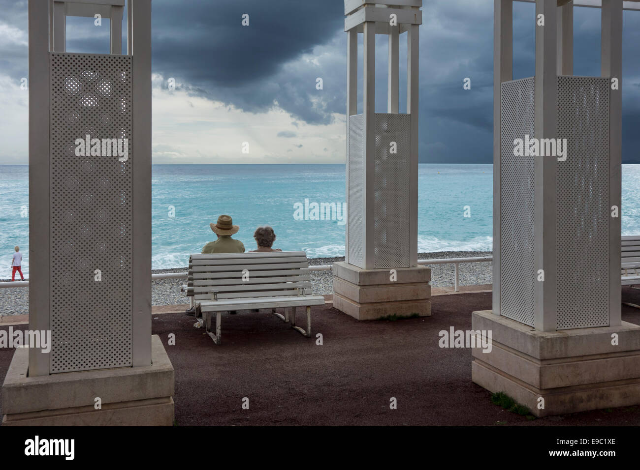 Coppia di anziani seduti sul banco a promenade e guardare scuro, minacciano pioggia nuvole sopra il Mar Mediterraneo a Nizza Francia Foto Stock