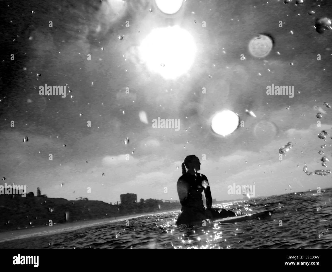 Surfer Girl in attesa in acqua con sun dietro di lei e spruzzi d'acqua intorno in bianco e nero Foto Stock