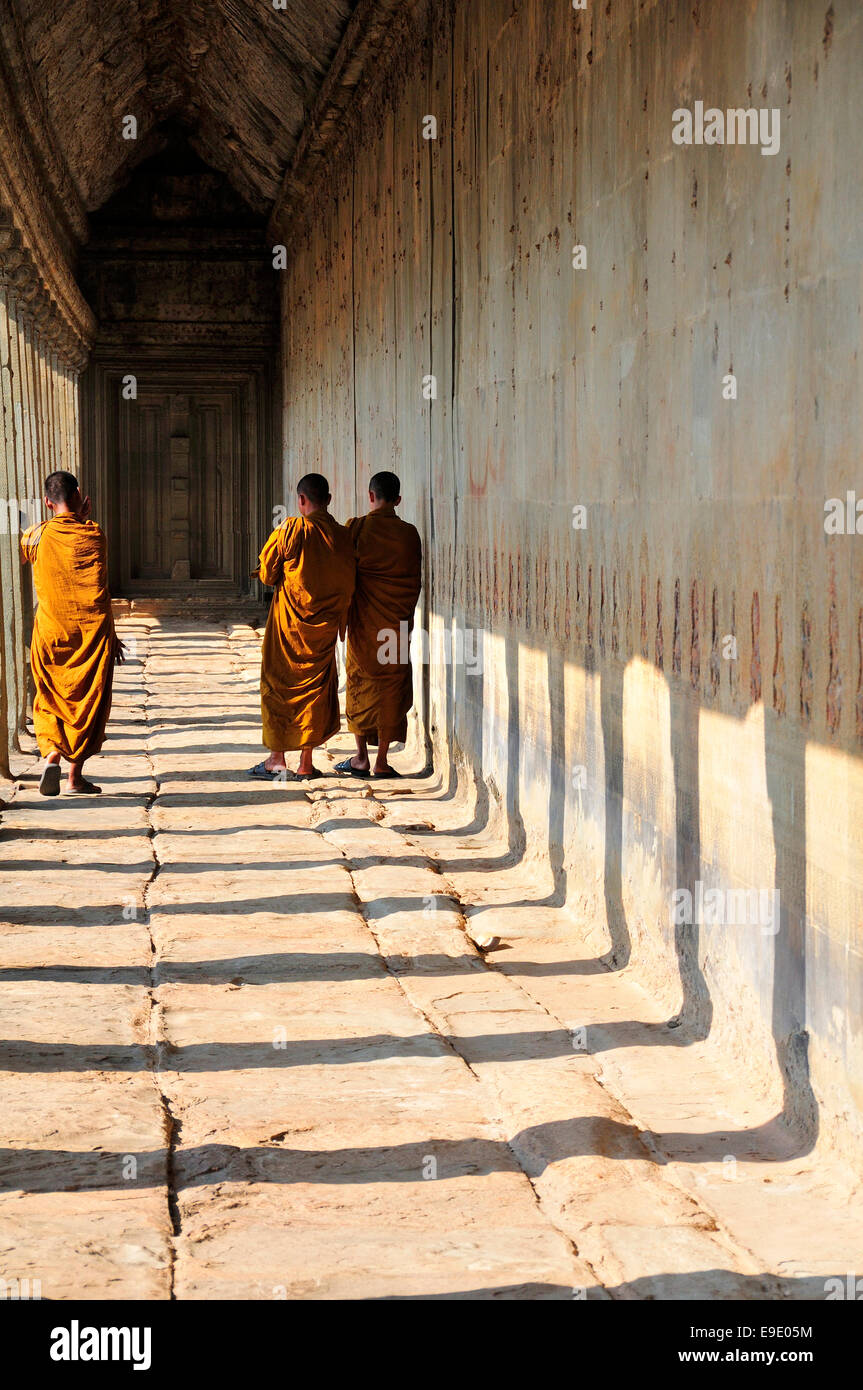 I monaci nelle vesti di colore giallo di passeggiare lungo la passerella all'entrata di Angkor Wat, un sito Patrimonio Mondiale dell'Unesco a Siem Reap, Cambogia, sud-est asiatico Foto Stock