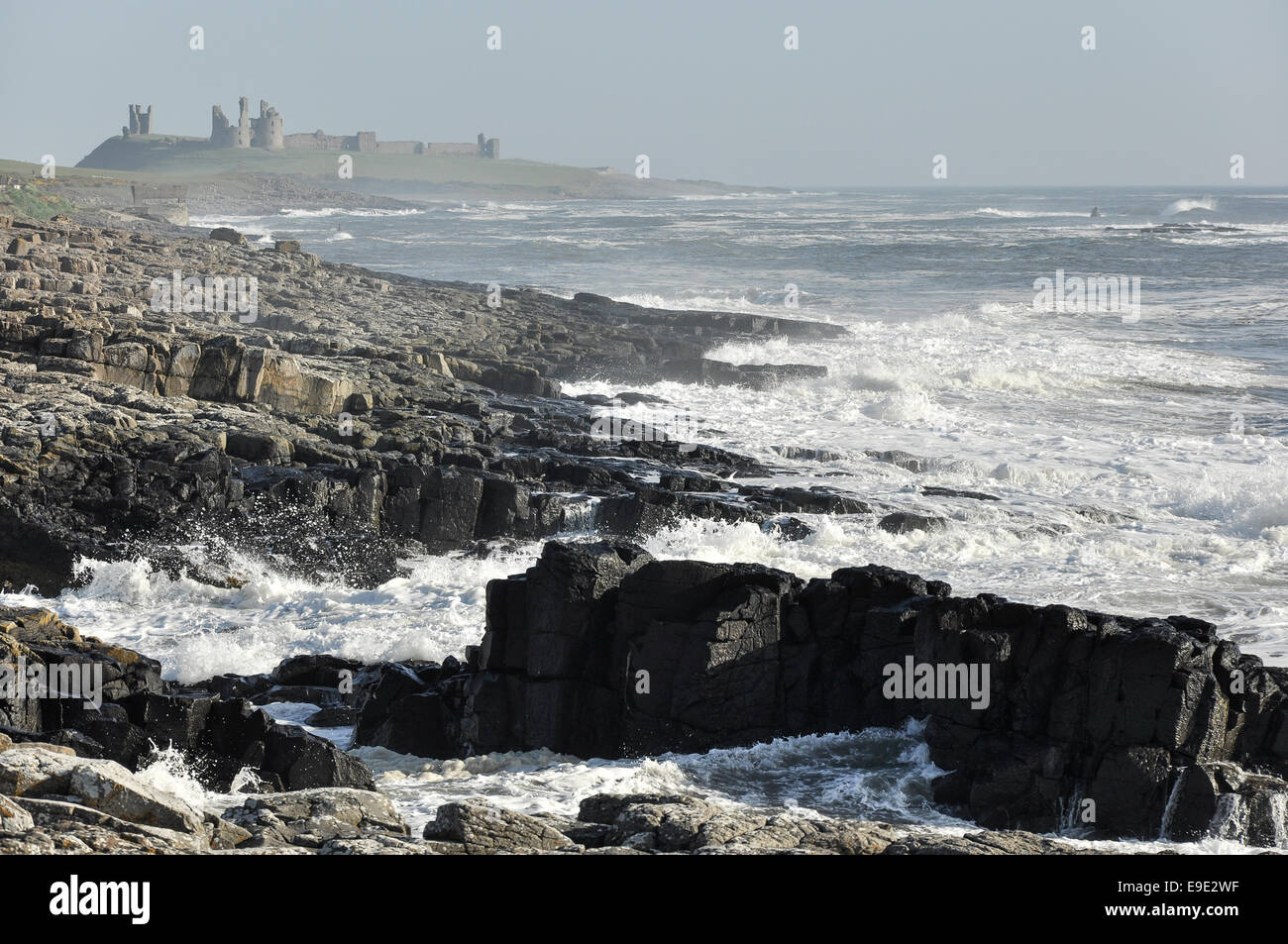 Luminose e breezy day con le onde che si infrangono sulle rocce vicino castello Dunstaburgh, Northumberland. Foto Stock