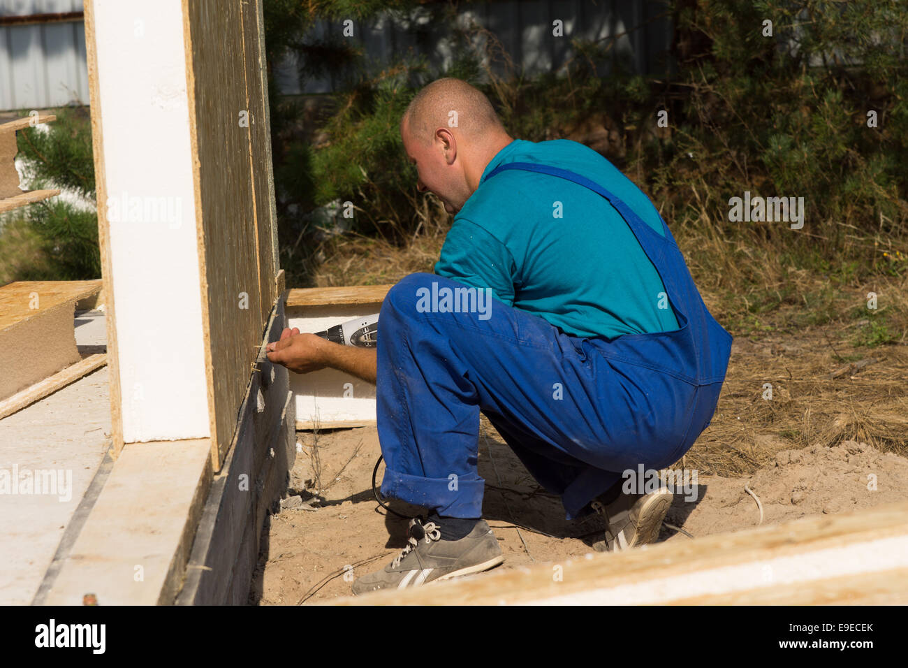 Workman installazione di pareti isolate su un sito di costruzione in ginocchio sul terreno per allineare la parte inferiore del pannello Foto Stock