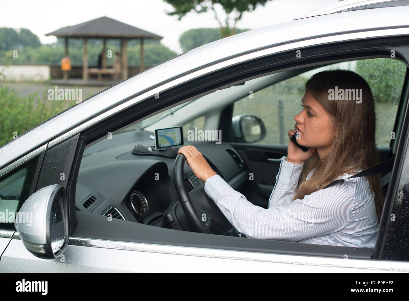 Azienda giovane donna alla guida di una vettura e parlando al telefono cellulare Foto Stock