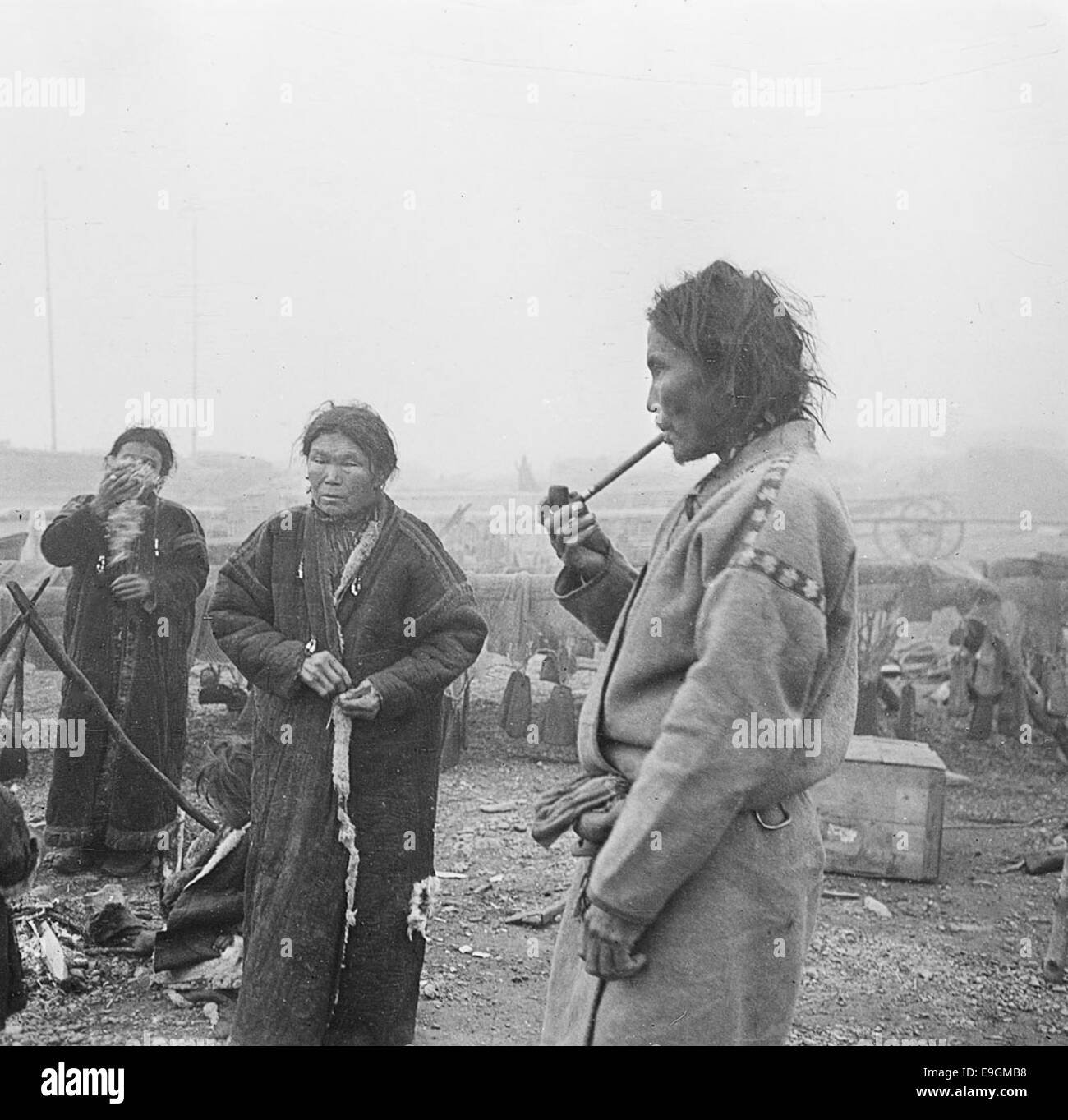 Questa fotografia mostra un uomo Jenisejostjak che fuma una pipa accanto a due donne, probabilmente di una comunità tradizionale in Russia. L'immagine cattura un momento di significato culturale, mostrando l'abbigliamento e le usanze di questo gruppo indigeno. Foto Stock