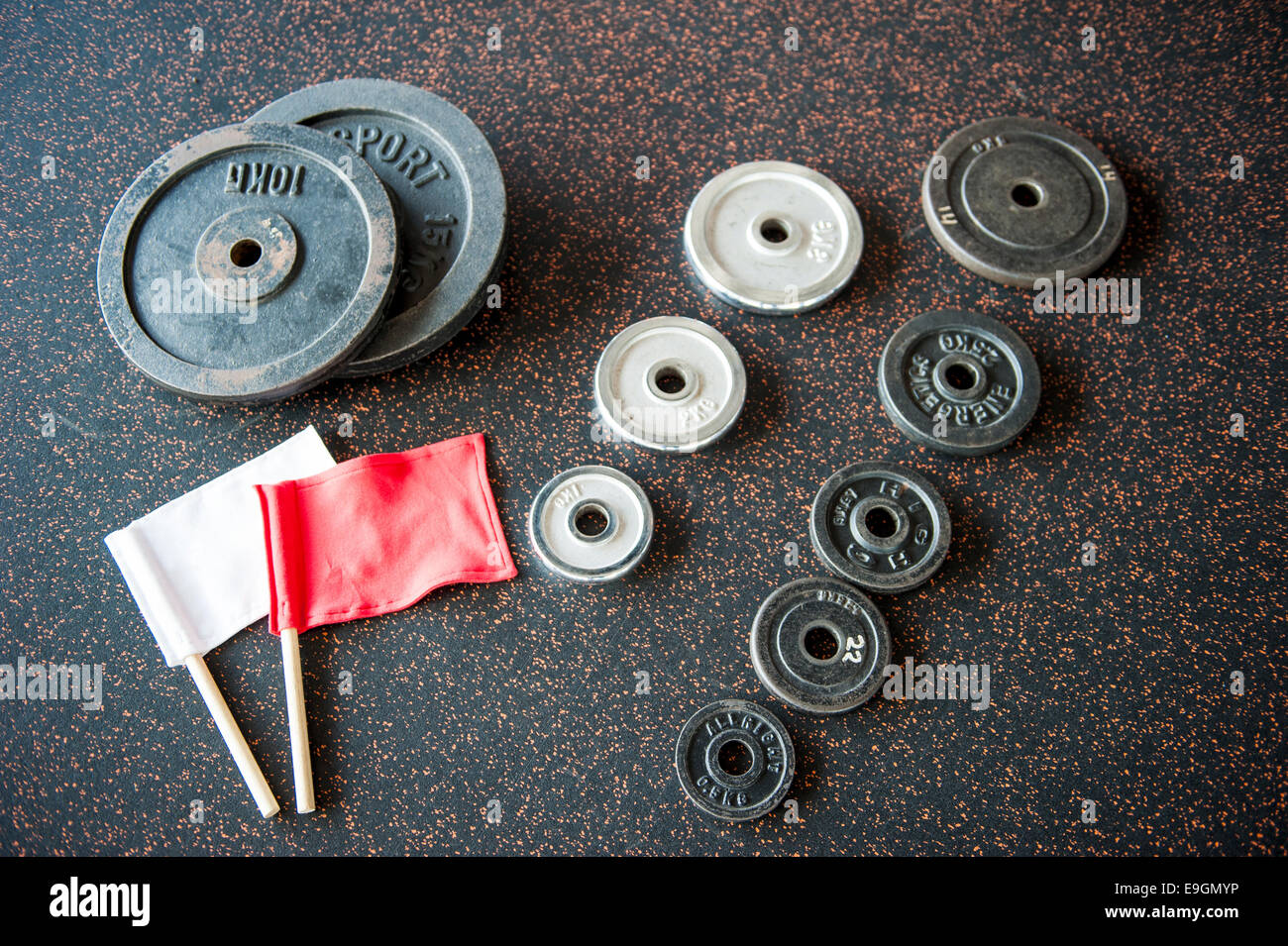 Set di pesi piastre di peso con il rosso e bianco arbitro bandiere disposti sul pavimento nero Foto Stock