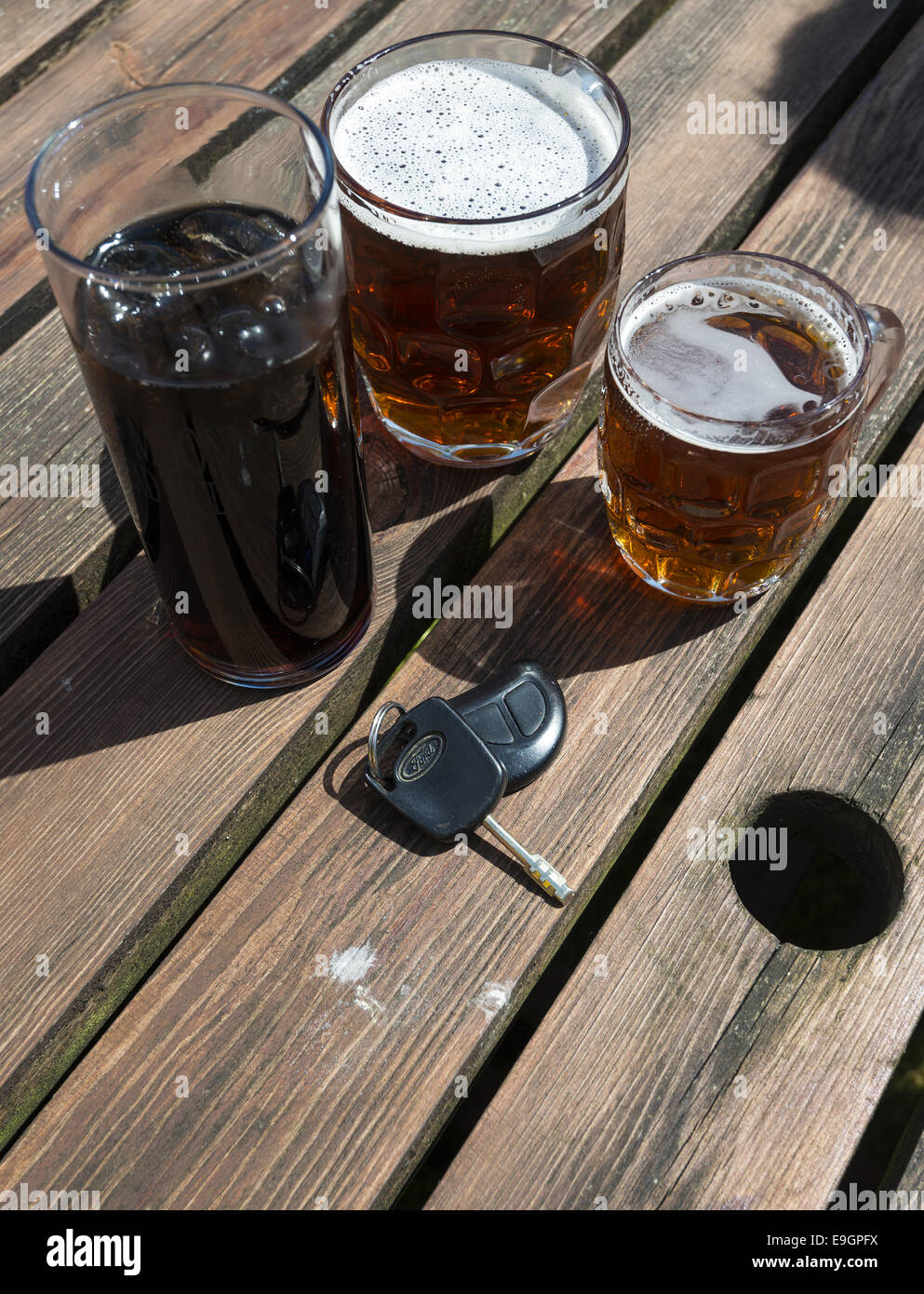 Chiavi auto con una bibita e pinte di birra su una birra in legno Tavolo da giardino Foto Stock