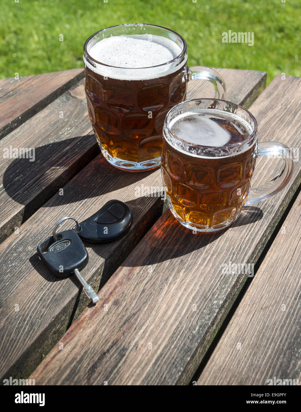 Le chiavi dell'auto e pinte di birra su una birra in legno Tavolo da giardino Foto Stock