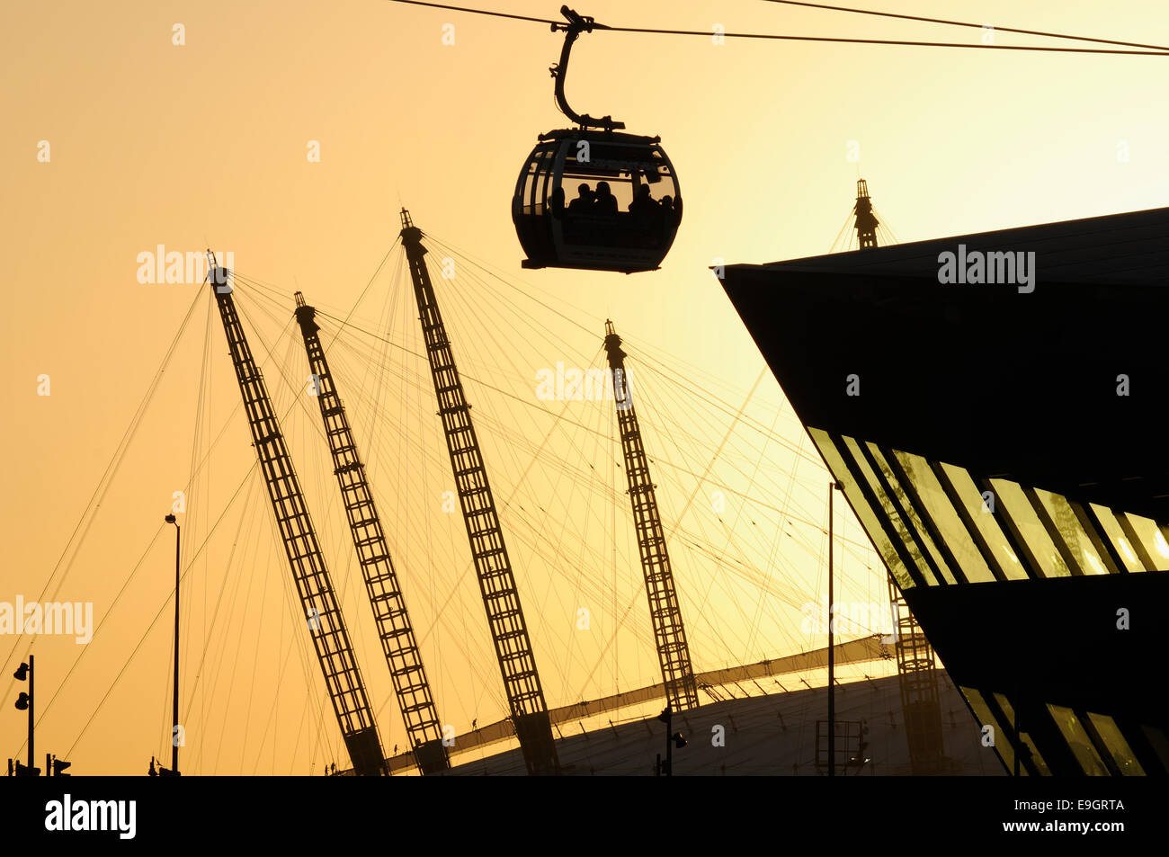 Docklands di Londra con Emirates funivia, O2 Arena e il palazzo di cristallo in silhouette al tramonto, contro il cielo arancione Foto Stock