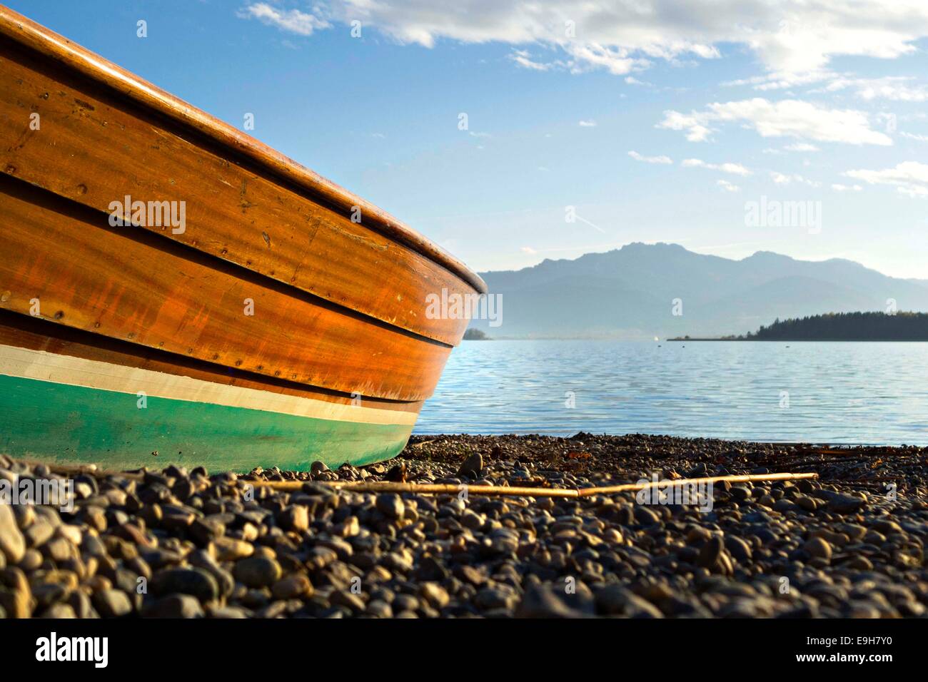 Basso prospettica di un gommone sulla spiaggia in pietra con vista sul lago per le Alpi bavaresi, Chiemsee, Chiemgau, Alta Baviera Germania Europa Foto Stock