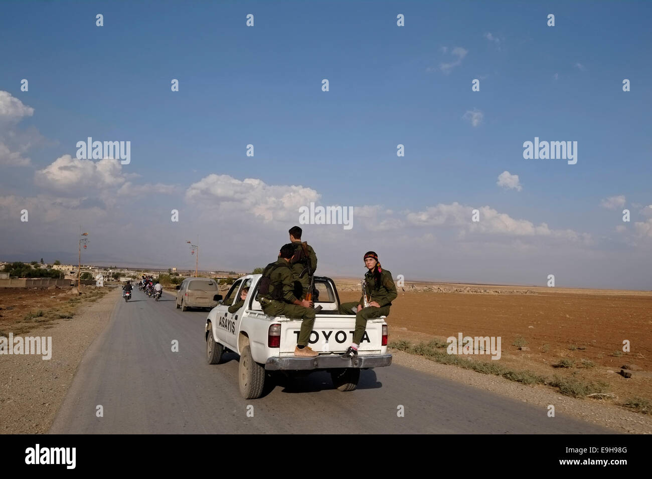 Membri armati del le forze di sicurezza interna noto anche come Asayish Asayis o delle regioni autonome all'interno della lingua curda amministrazione autonoma del nord ed est della Siria a cui spesso viene fatto riferimento come Rojava cavalcare un open-backed Toyota pickup truck in Al Hasakah o Hassakeh nella Siria settentrionale Foto Stock