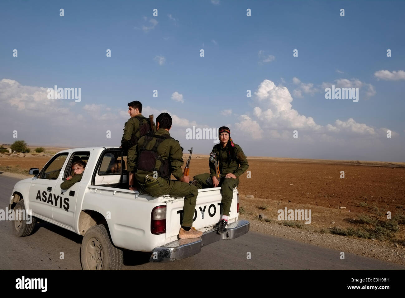 Membri armati del le forze di sicurezza interna noto anche come Asayish Asayis o delle regioni autonome all'interno della lingua curda amministrazione autonoma del nord ed est della Siria a cui spesso viene fatto riferimento come Rojava cavalcare un open-backed Toyota pickup truck in Al Hasakah o Hassakeh nella Siria settentrionale Foto Stock
