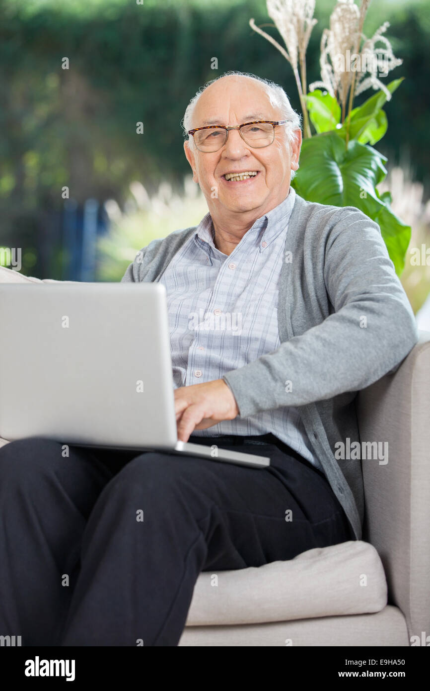 Felice senior uomo seduto con il computer portatile sul lettino Foto Stock