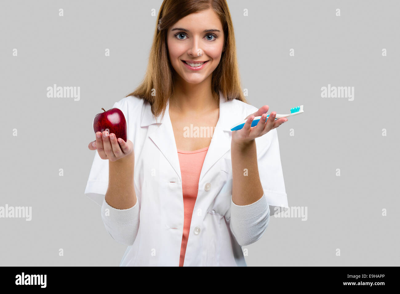 Bello e attraente dentista femmina azienda strumenti e una mela rossa, isolato su uno sfondo bianco Foto Stock