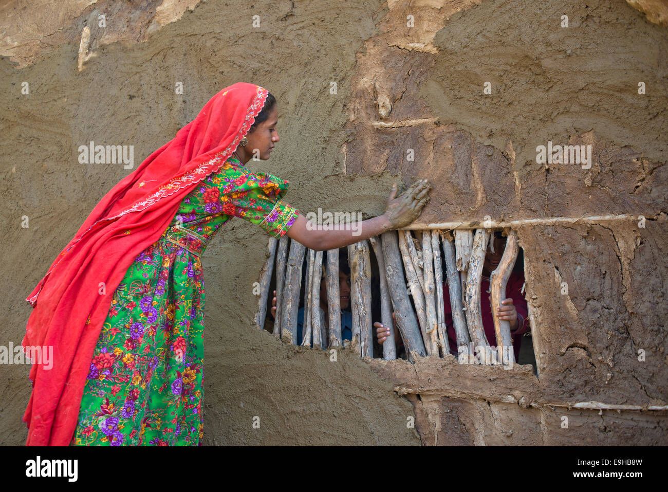 Ragazza in abito tradizionale intonacare il muro di una casa con una miscela di acqua e di sabbia e sterco di vacca, Rann di Kutch, Gujarat Foto Stock