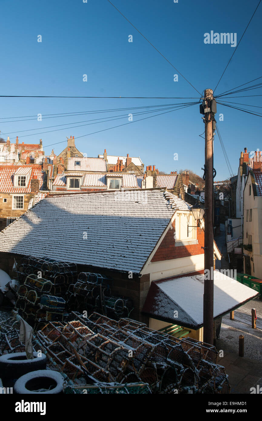 Tetti spolverati di neve e vasi di aragosta impilati a Robin Hood's Bay, Yorkshire, sotto i cieli invernali limpidi e vecchi cavi telegrafici Foto Stock