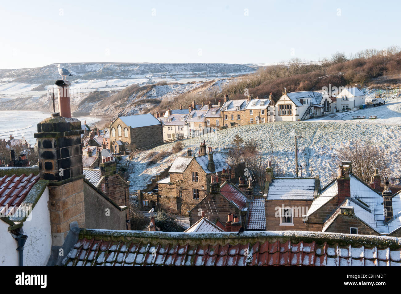 Tetti spolverati di neve e vasi di aragosta impilati a Robin Hood's Bay, Yorkshire, sotto i cieli invernali limpidi e vecchi cavi telegrafici Foto Stock