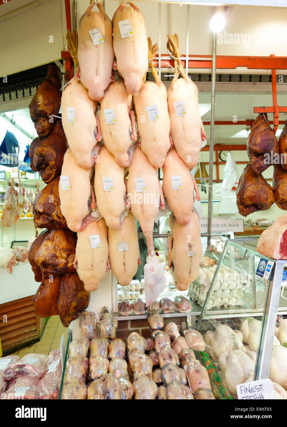 I prosciutti e le oche spennate appendere al di fuori di una macelleria a Oxford il mercato coperto pronto per Natale Foto Stock