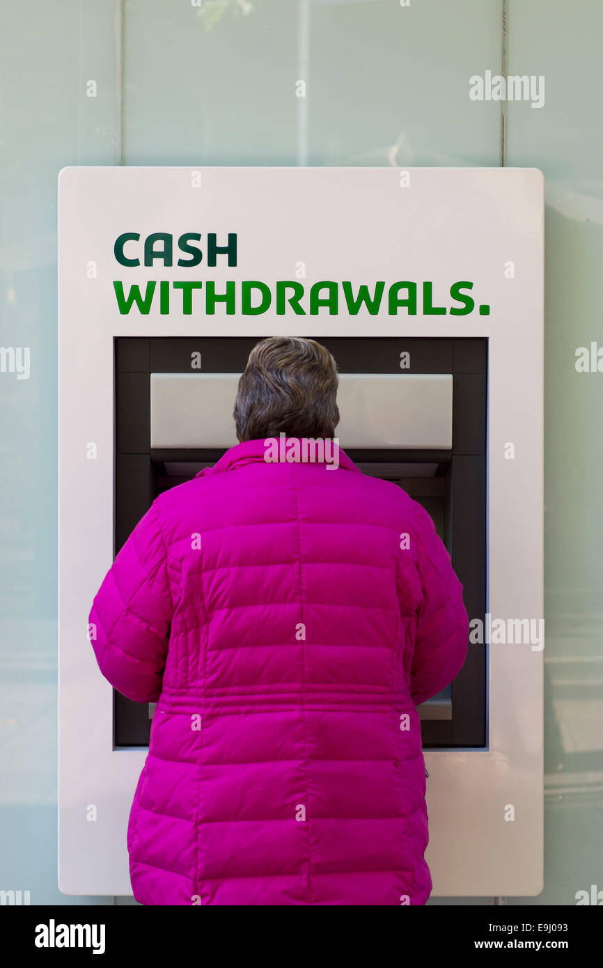 Una donna si avvale di una banca bancomat (ATM) per ritirare i soldi. Foto Stock
