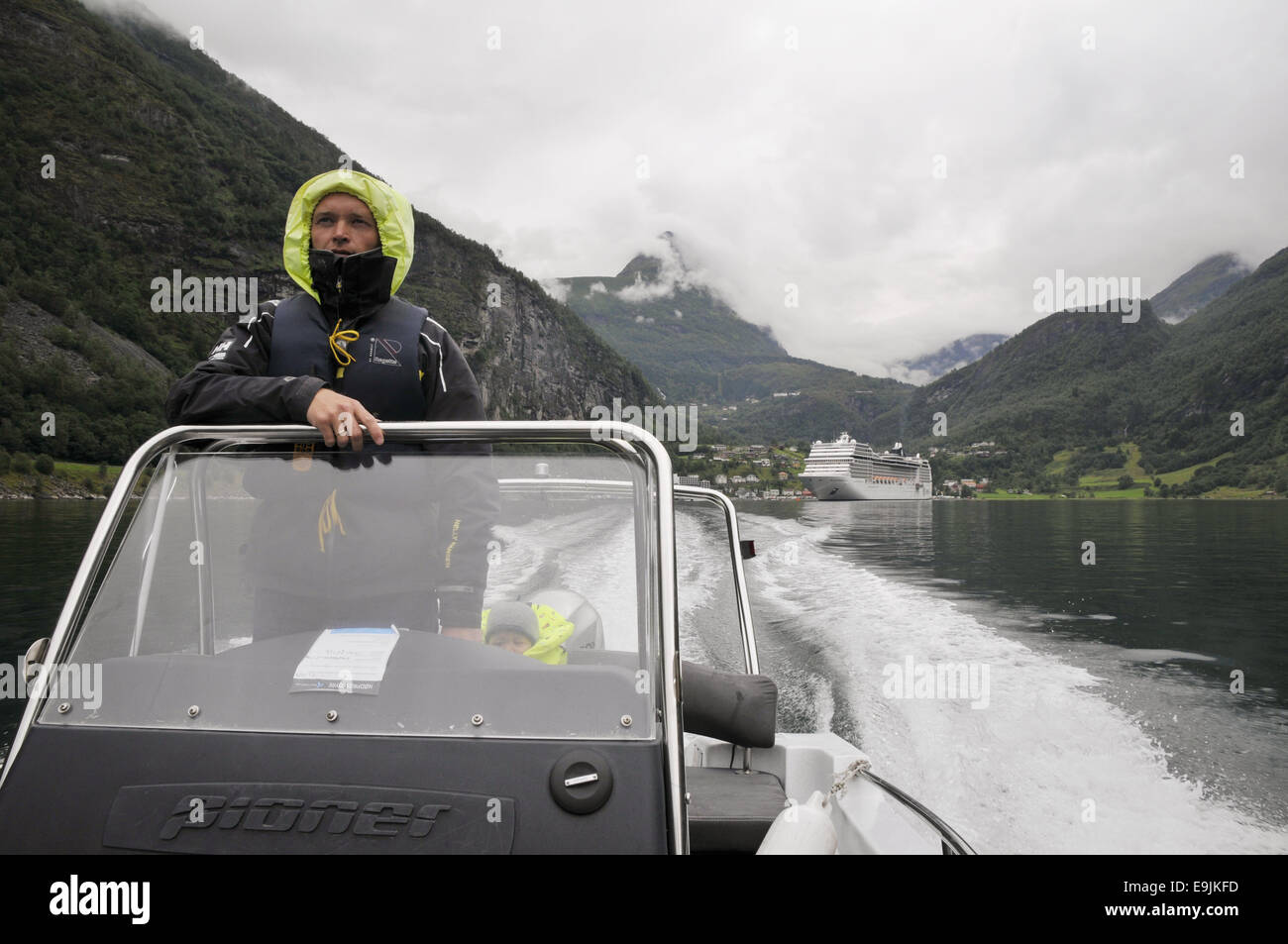 Un taxi imbarcazione andando fuori il Geiranger fjord, Norvegia, sulla strada per Skageflå. Una nave da crociera è ormeggiata al porto di Geiranger. Foto Stock