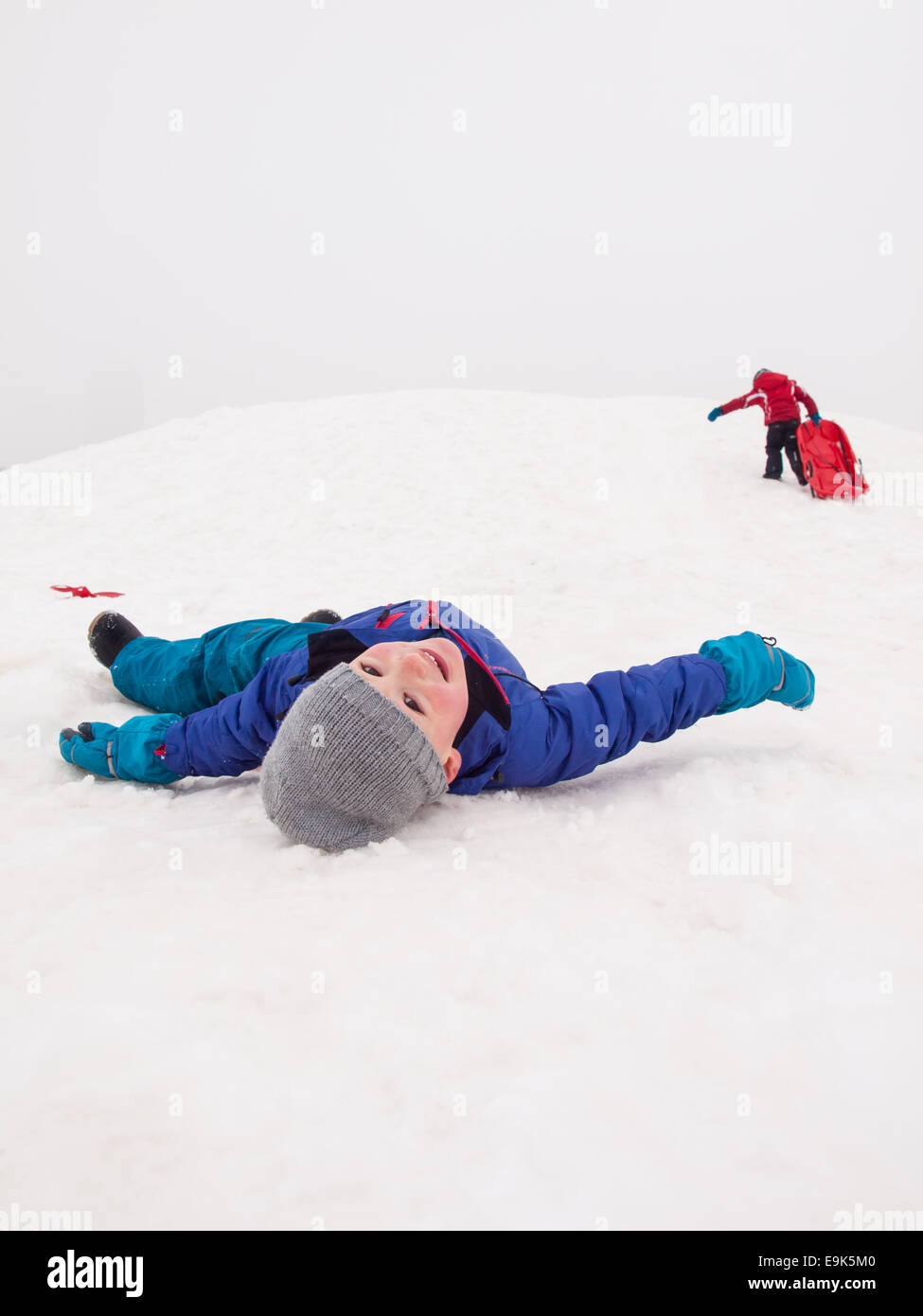 Piccolo Ragazzo sorridente giacente sulla neve nella parte inferiore di una slitta hill Foto Stock