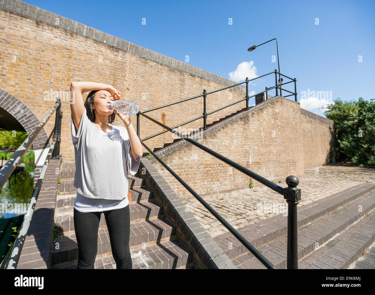 Stanco giovane donna acqua potabile su scale Foto Stock