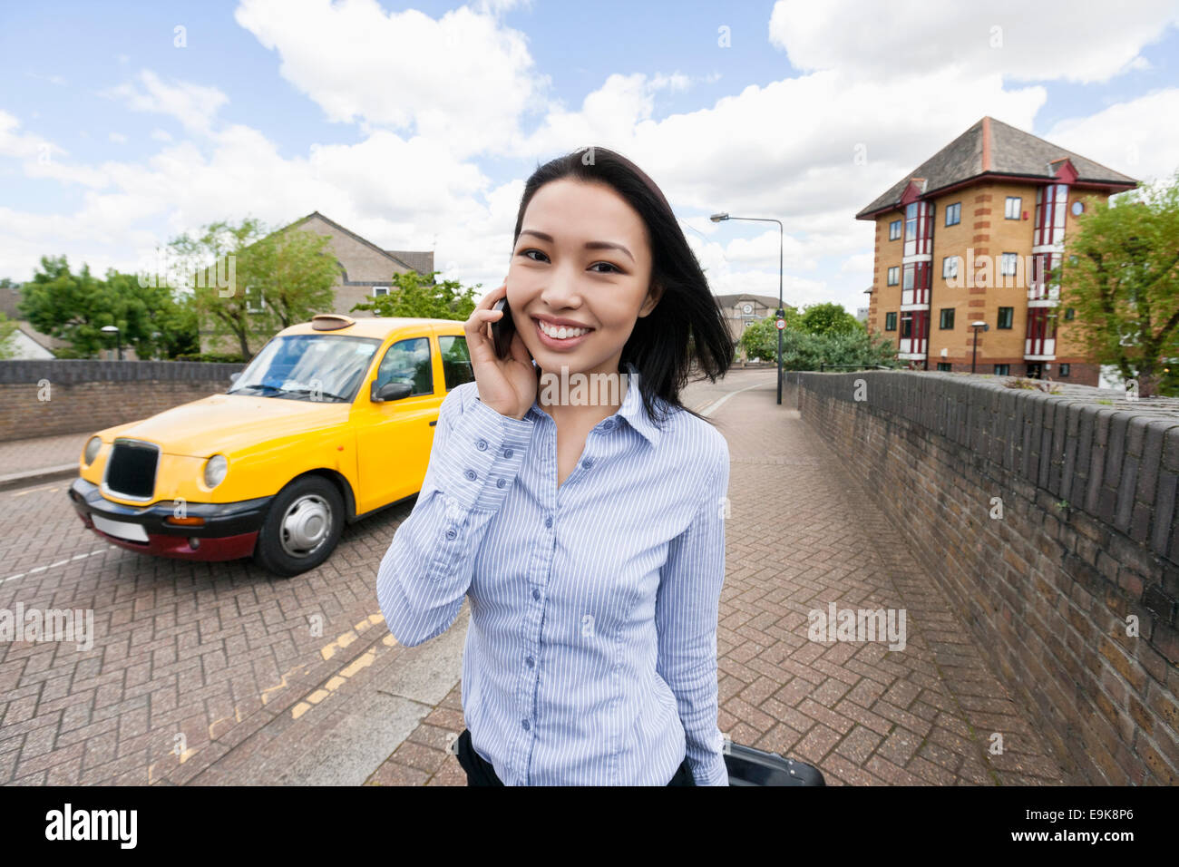 Ritratto di sorridere imprenditrice risposta cellulare sul marciapiede con il taxi in background Foto Stock
