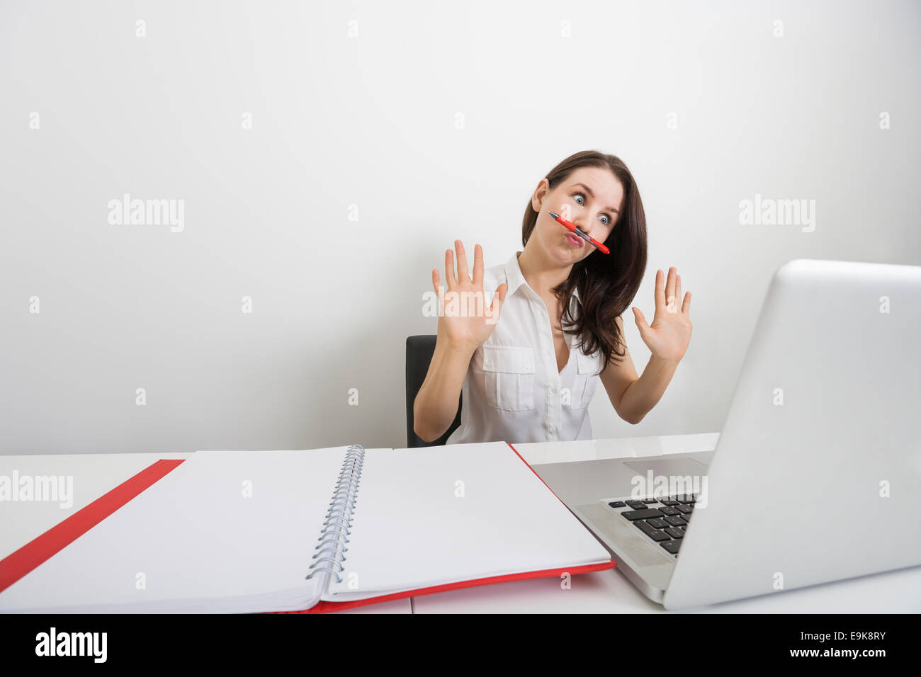 Stupito imprenditrice guardando laptop tenendo la penna sotto il naso di office Foto Stock