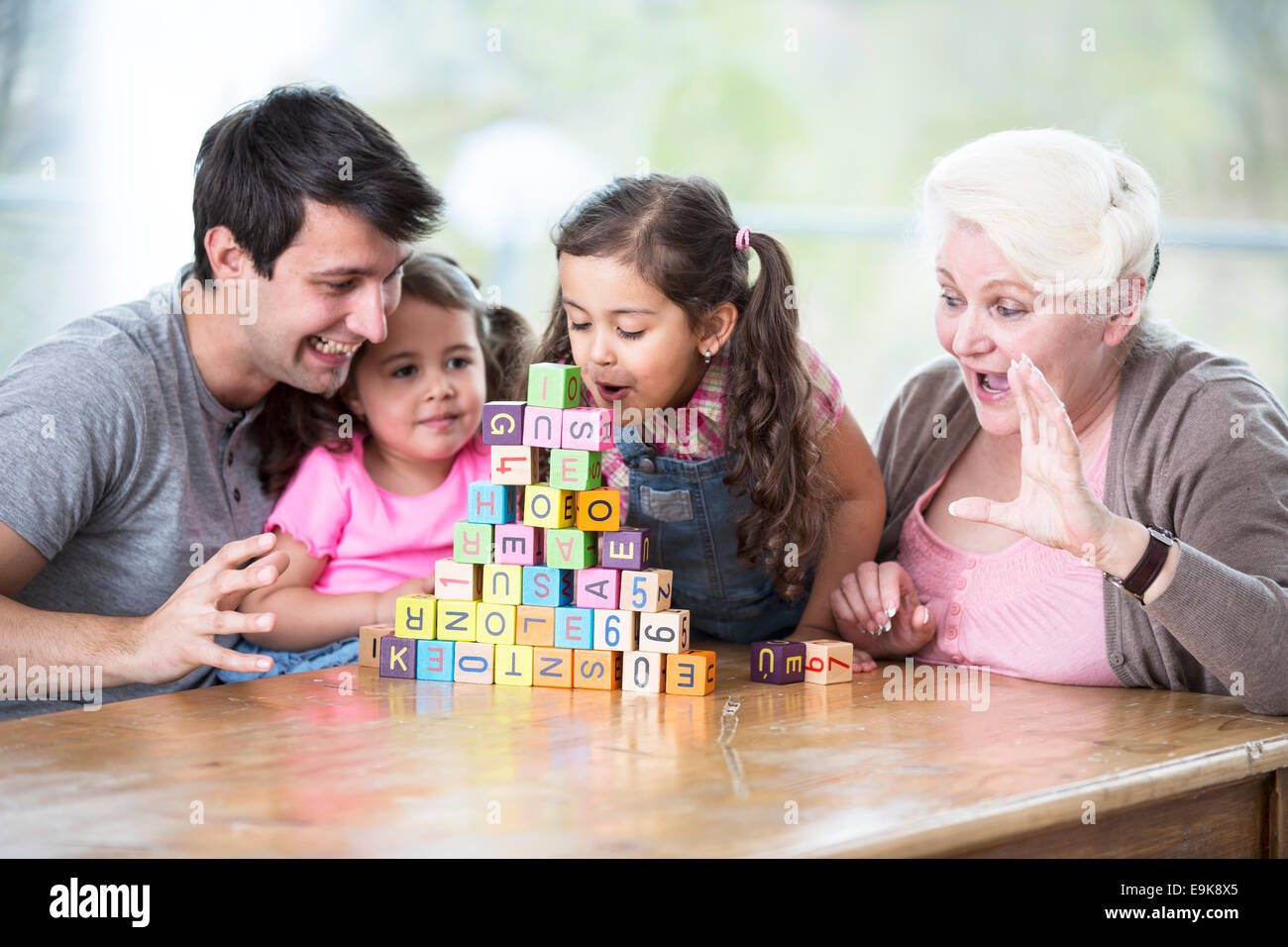 Ragazza carina di soffiaggio blocchi alfabeto mentre la famiglia sta guardando in casa Foto Stock