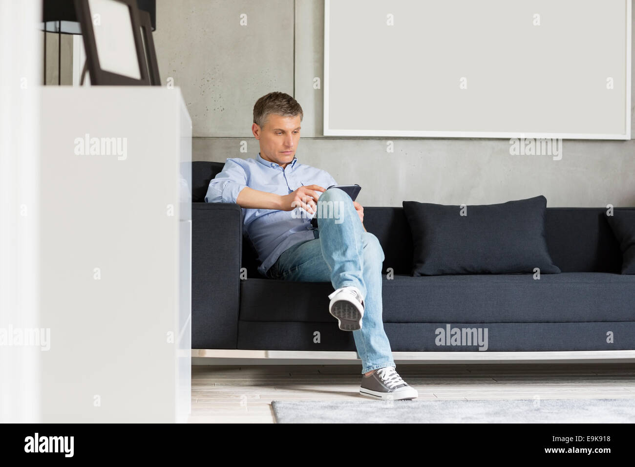 Lunghezza intera di uomo di mezza età con tavoletta digitale sul divano Foto Stock