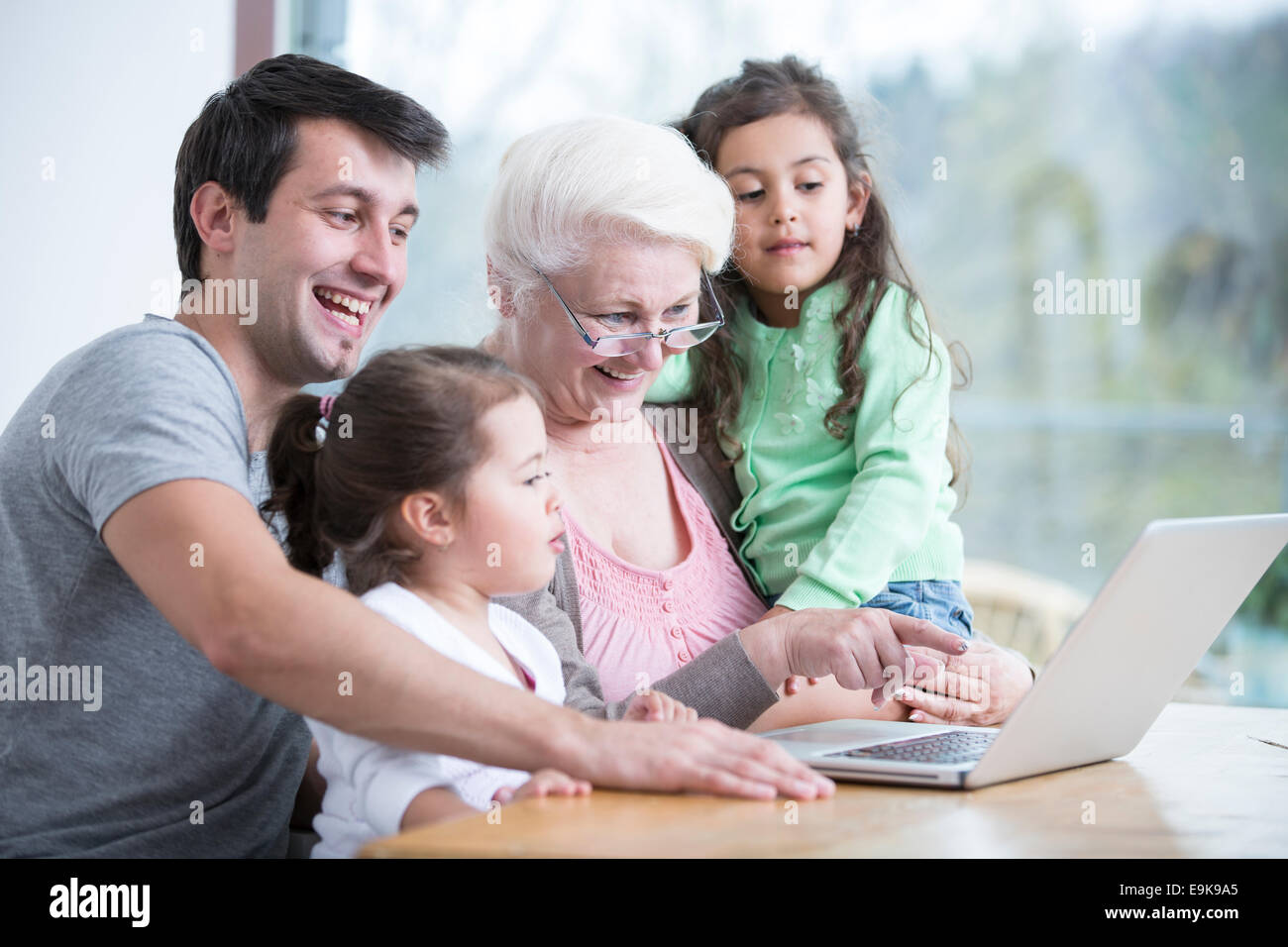 Felice tre generazioni la famiglia tramite computer portatile a tavola in casa Foto Stock