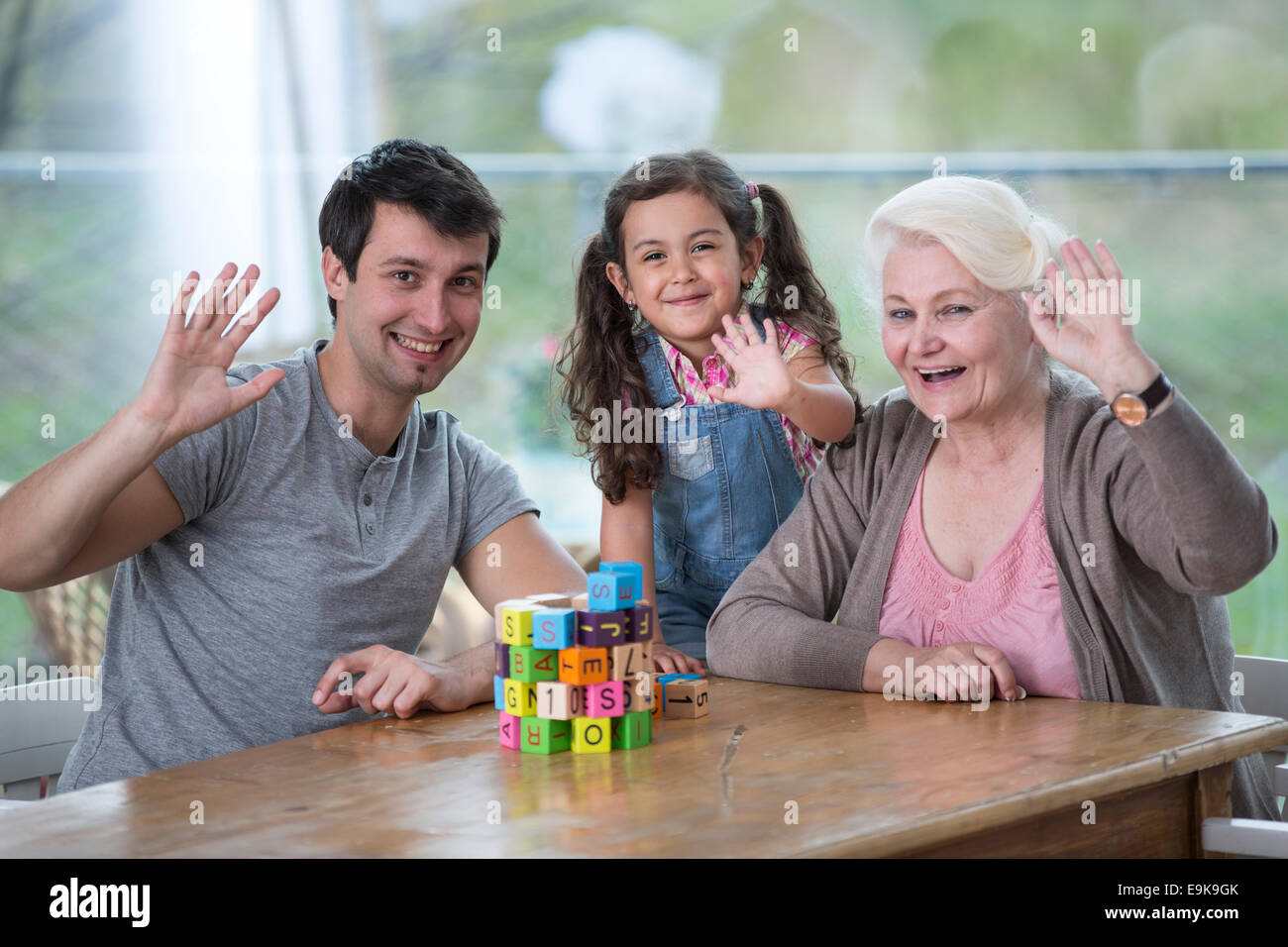 Ritratto di donna senior con il figlio e la nipote sventolare le mani a tavola Foto Stock