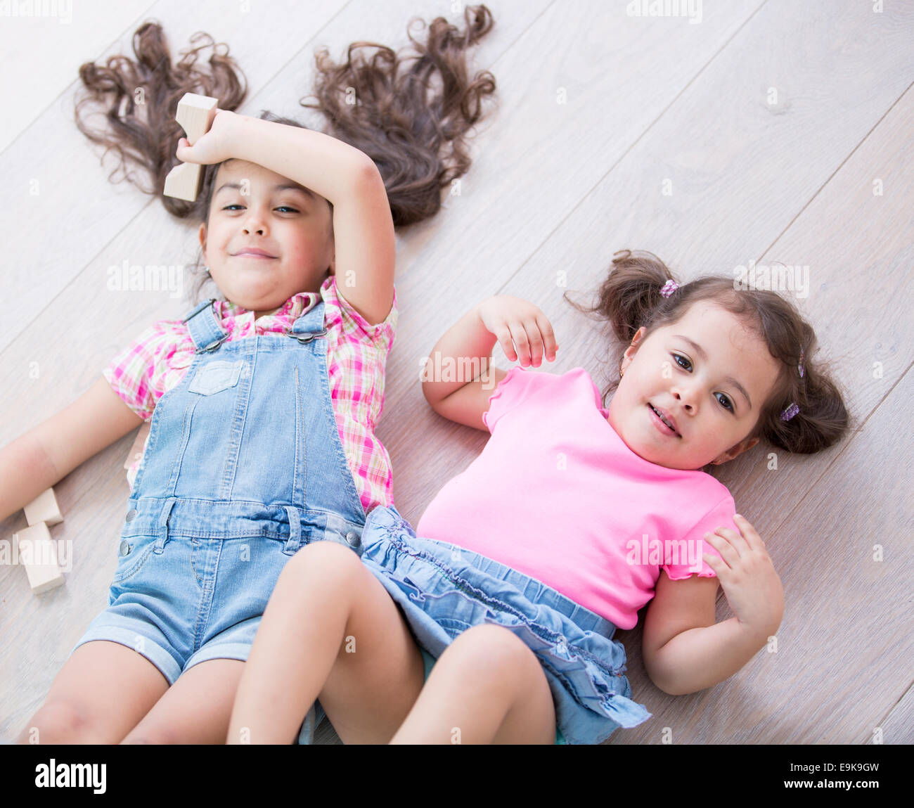 Angolo di alta vista di carino piccole sorelle sdraiato sul pavimento in legno a casa Foto Stock
