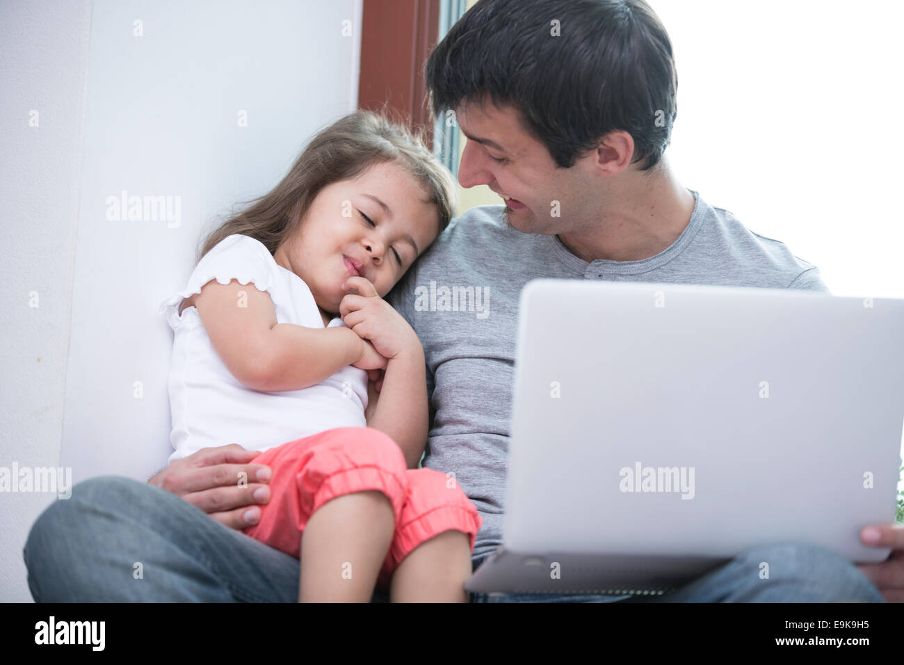 Padre Felice guardando carino figlia dormendo mentre utilizzando portatile a casa Foto Stock