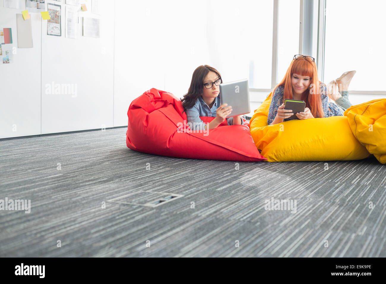 Imprenditrici utilizzando compresse digitale mentre vi rilassate sulle sedie beanbag nel creative office Foto Stock