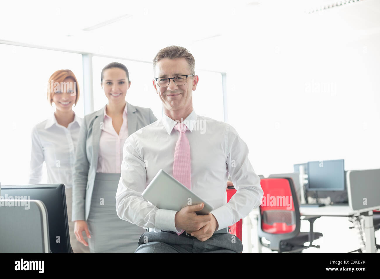 Ritratto di happy businessman holding tablet PC con le colleghe in background in ufficio Foto Stock