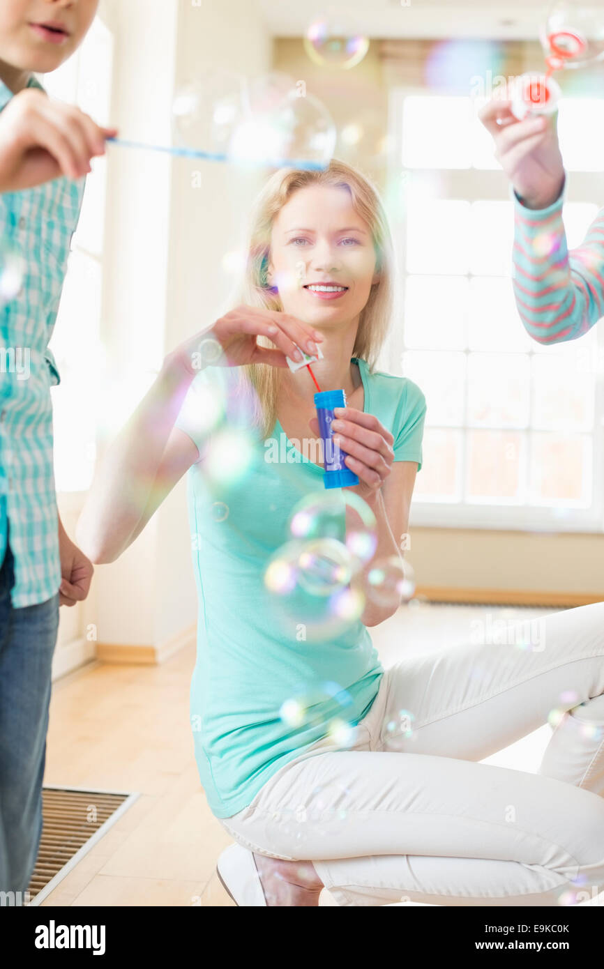 Felice madre e bambini che giocano con bacchette di bolle a casa Foto Stock
