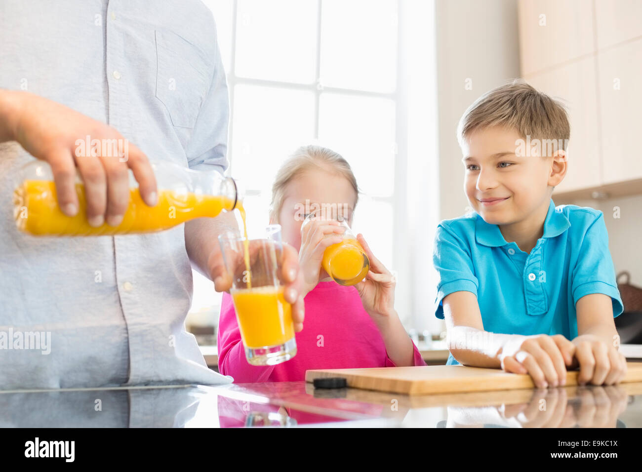 Sezione mediana del padre che serve il succo d'arancia per i bambini in cucina Foto Stock