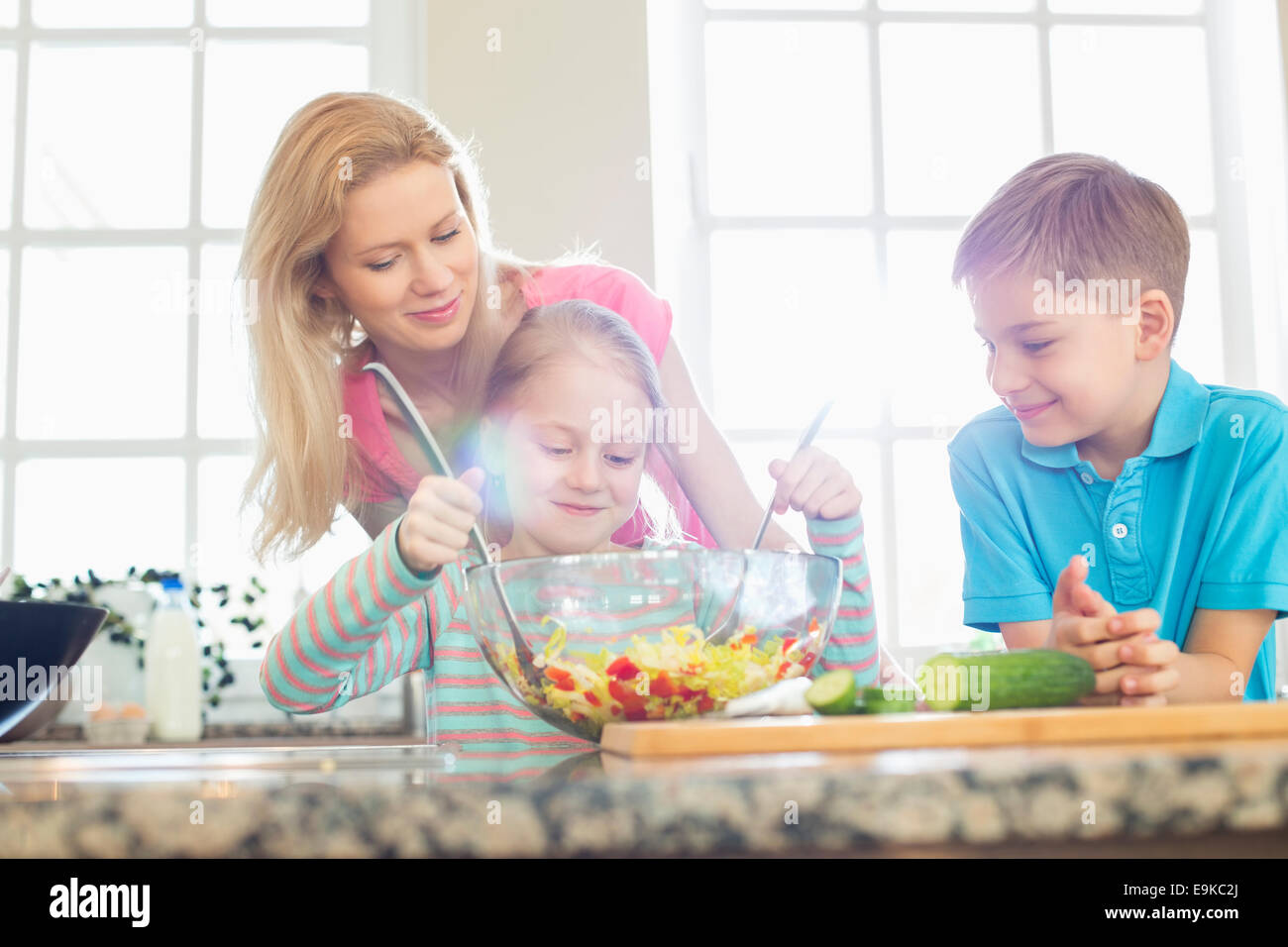 Famiglia guardando ragazza insalata di miscelazione in cucina Foto Stock