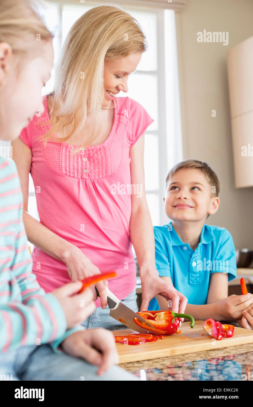 Donna felice tritare il peperone rosso permanente, mentre con i bambini in cucina Foto Stock