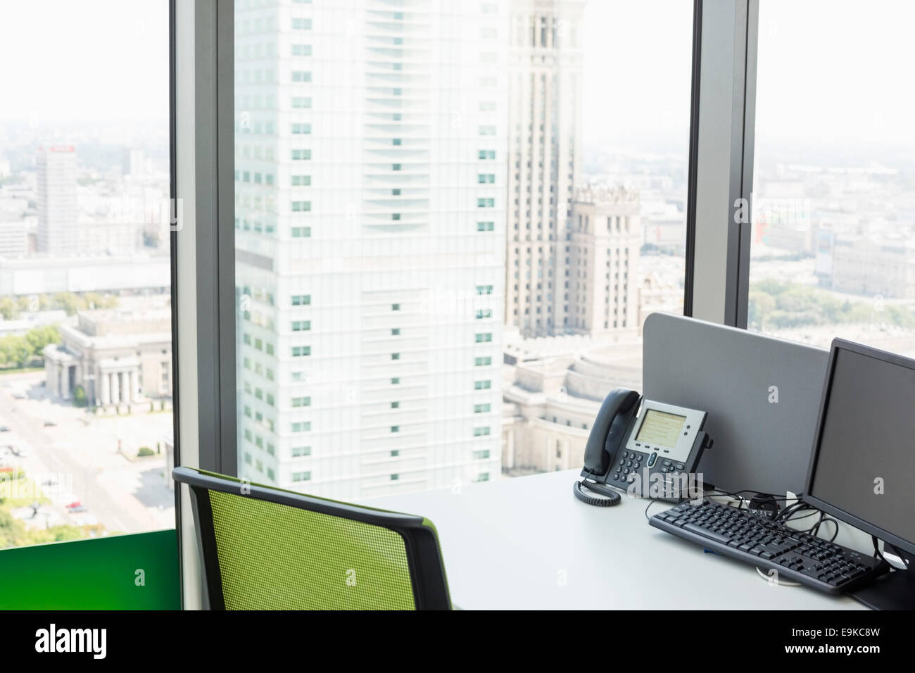 Computer desktop e il telefono sulla scrivania dalla finestra di vetro in office Foto Stock