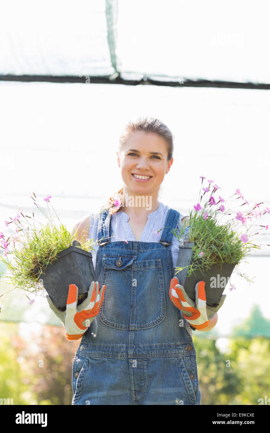 Ritratto di felice giardiniere femmina azienda vasi di piante in serra Foto Stock